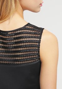 Haut sans manches noir avec un dos en maille texturée à rayures horizontales et un tissu uni sur le devant.