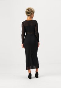 Juoda, ilgomis permatomomis rankovėmis su prigludusia liemene. Ilgis iki grindų, su subtiliu plyšiu nugaroje. Avėti su juodais aukštakulniais.