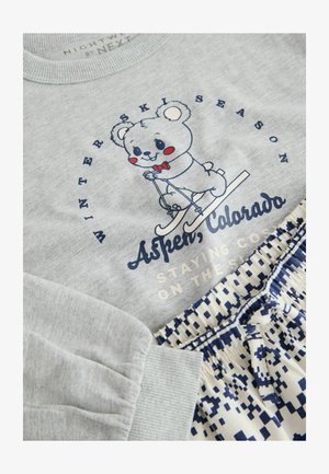 Hanorac gri cu un ursuleț de desene animate pe schiuri, având textul "Sezonul de schi de iarnă Aspen, Colorado". Asortat cu pantaloni scurți albi cu modele geometrice albastre.