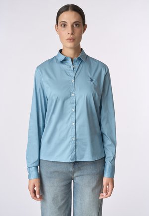 Camicia a maniche lunghe blu chiaro in tessuto liscio, con chiusura a bottoni sul davanti e un piccolo logo ricamato sul petto.