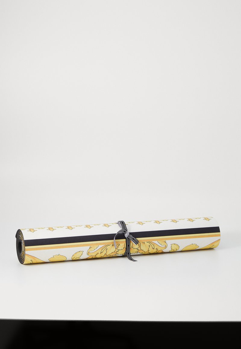 Válcované tapety s vzorem žlutých listů na bílém pozadí, zajištěné černo-bílou stuhou, s hladkou texturou.