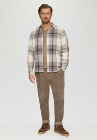 Geruite shirt in wit, grijs en paars, met een kraag en knoopsluiting. Gecombineerd met een bruine corduroy broek en bruine sneakers. Soepele textuur.