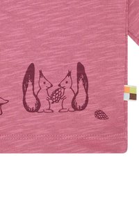 Rosa Stoff-T-Shirt, das zwei braune Eichhörnchen zeigt, die einen Tannenzapfen halten, mit einem kleinen Tannenzapfen-Detail in der Nähe und einem mehrfarbigen Etikett an der Seite.