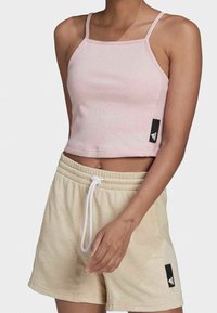 Růžový žebrovaný crop top s tenkými ramínky, spárovaný s béžovými šortkami s tkaničkou a černou značkovou cedulkou na boku. Měkká textura a přiléhavý střih.