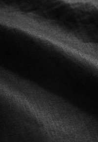 Tissu noir texturé avec un motif de tissage subtil, affichant des nuances variées dues à la réflexion de la lumière sur sa surface.