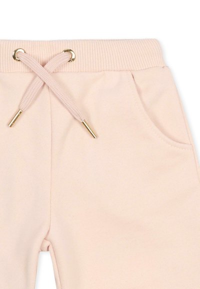 Pantalon de survêtement rose clair avec taille élastique côtelée, cordons croisés à embouts dorés et poche latérale à droite.