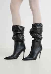 Schwarze Leder-Stiefeletten mit schlaffem oberen Design, spitz zulaufenden Zehen und schlanken Stiletto-Absätzen. Glatte Textur mit glänzender Oberfläche.