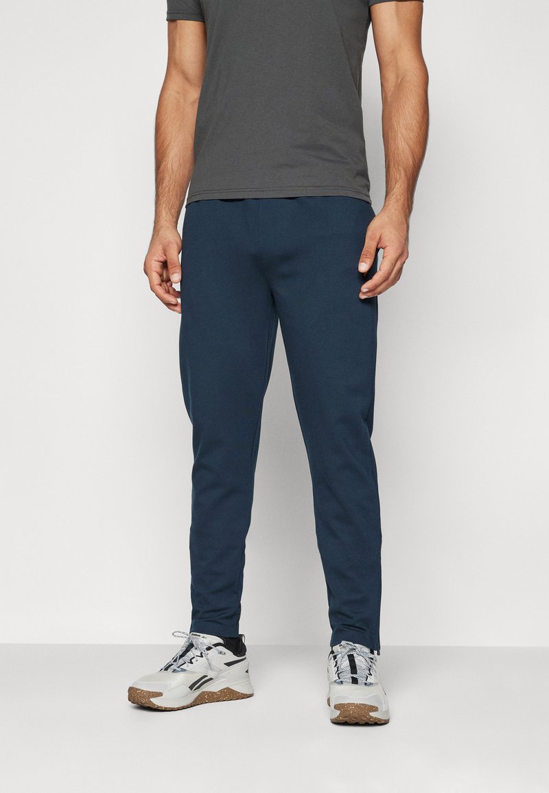 Navy blue joggers with a slim fit design, made from soft fabric; paired with gray sports shoes featuring white accents and textured soles.