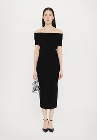 Black off-shoulder fitted dress, midi length, made from smooth fabric. Paired with a silver transparent handbag and black heeled shoes.