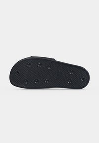 Black sandal sole with raised circular grips and a textured diamond pattern on a plain light background.