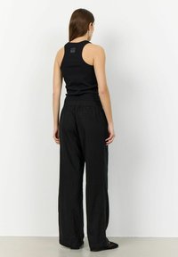 Svart linne som kombineras med löst sittande svarta byxor. Linne har en åtsittande design, medan byxorna har en elasticerad midja och texturerad tyg.