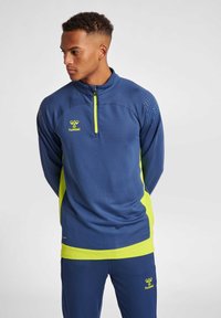 Marinblå sportströja med kvartslång dragkedja och gula accenter, texturerad axeldetalj och logotyp. Matchas med marinblå byxor som också har gula detaljer.