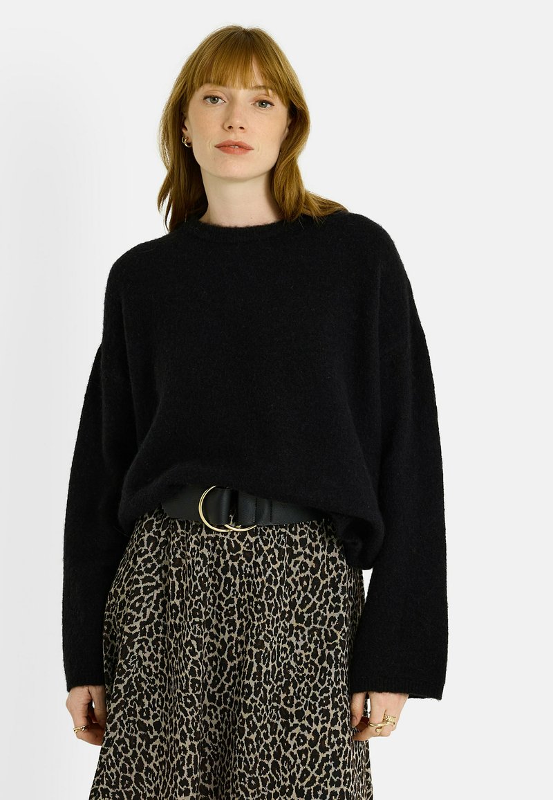 Pull noir surdimensionné en maille avec un col rond et des épaules tombantes, associé à une jupe imprimé léopard, cintrée par une ceinture noire.