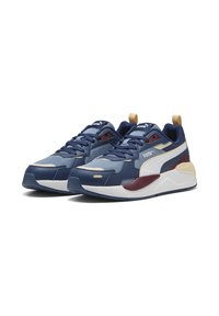 Baskets de sport bleues avec un matériau texturé, accents contrastants en blanc et bordeaux, semelle épaisse et languette rembourrée. Les éléments de design uniques incluent un onglet arrière.