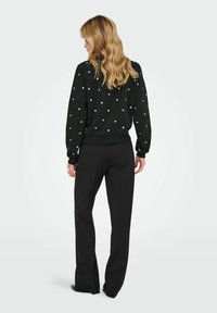 Zwarte sweatshirt met gouden hartpatronen, gecombineerd met zwarte wijde broek. Heeft ribgebreide manchetten en zoom, zachte stoftextuur.