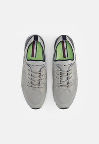 Jasnoszare buty sportowe z siateczkowymi wstawkami, srebrnymi akcentami, czarną podeszwą i zieloną wyściółką. Sześć otworów na sznurowadła z sznurówkami i etykieta marki.