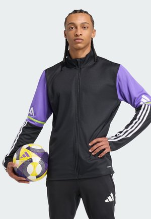 Zwarte trackjas met paarse mouwen, witte Adidas-strepen en een slim fit; houdt een getextureerde gele en paarse voetbal vast.