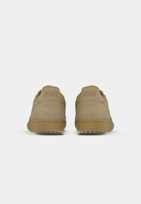 Een paar tan Nike sneakers gezien vanaf de achterkant tegen een effen witte achtergrond.
