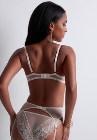 Ensemble de lingerie en dentelle beige comprenant un soutien-gorge semi-transparent et une culotte taille haute avec des motifs floraux et des bretelles ajustables.