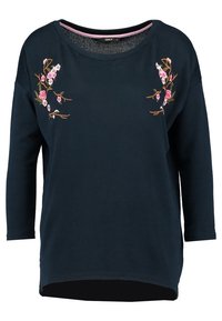 Navyblauw langemouw-shirt met roze bloemenborduurwerk op de schouders en een ronde halslijn met roze bies aan de binnenkant.