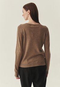 Pull en maille marron avec col rond, manches slim, poignets et ourlet côtelés. Texture douce, coupe ajustée et détails de coutures minimaux.