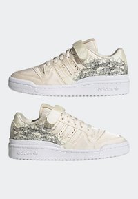 Beige sneakers with a satin finish, featuring three white stripes, a Velcro strap, and black floral outlines on the sides. White rubber sole.