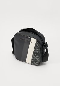 Svart crossover-veske med blank finish, med en hvit vertikal stripe og gjentatt logomuster i mørkegrått. Glidelås-lukking, justerbar stropp.