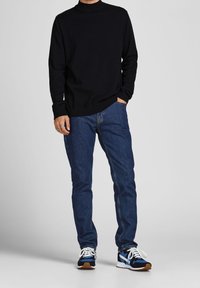 Pull en coton noir à col montant, associé à un jean en denim bleu et des baskets bleues avec des accents blancs et marron.