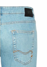 Jasnoniebieskie dżinsy mają tylną kieszeń z ozdobnym przeszyciem i czarną metkę marki przy pasie.