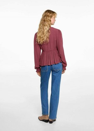 Bordeauxrote Bluse mit langen Ärmeln und plissiertem Rückendetail, kombiniert mit blauen gerade geschnittenen Jeans und beigen High Heels.