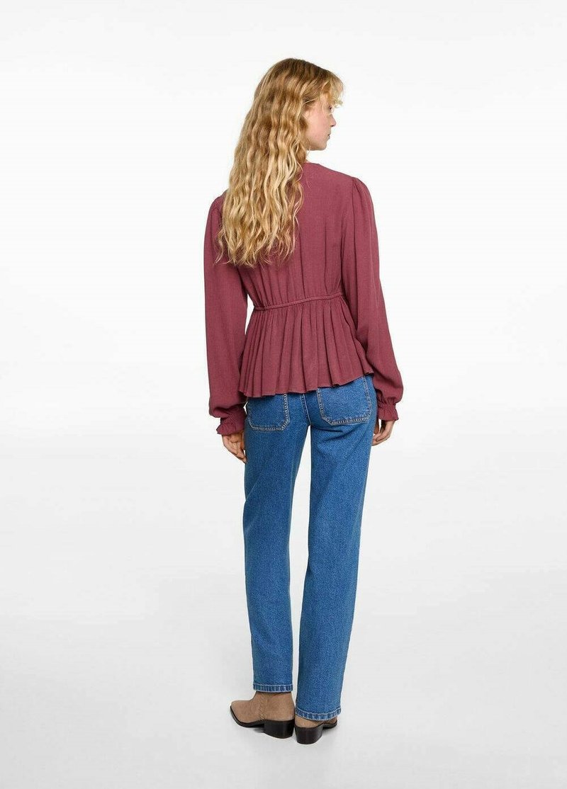 Bordeauxrote Bluse mit langen Ärmeln und plissiertem Rückendetail, kombiniert mit blauen gerade geschnittenen Jeans und beigen High Heels.