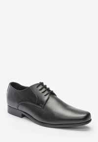 Chaussure habillée en cuir noir avec une texture lisse, bout rond, design à lacets et détails de couture minimalistes. Semelle en caoutchouc plate.
