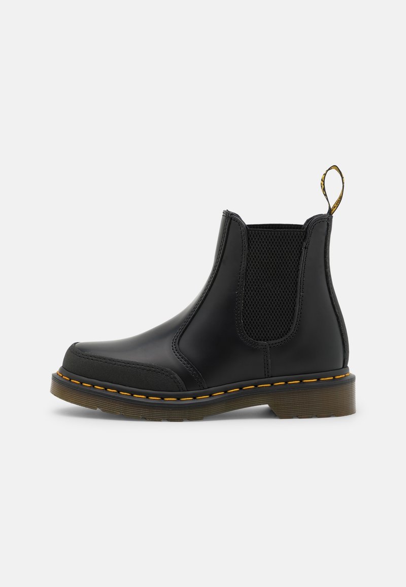 Bottine Chelsea en cuir noir avec panneaux latéraux élastiques, couture jaune sur la semelle et languette à l'arrière.