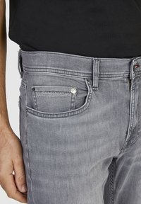 Jean en denim gris à coupe slim, avec une poche avant, un bouton métallique et des détails de couture subtils au niveau de la taille et des poches.