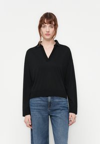 Black long-sleeve pullover with a V-neck and collar. Features a relaxed fit and ribbed hem. Worn with blue jeans.