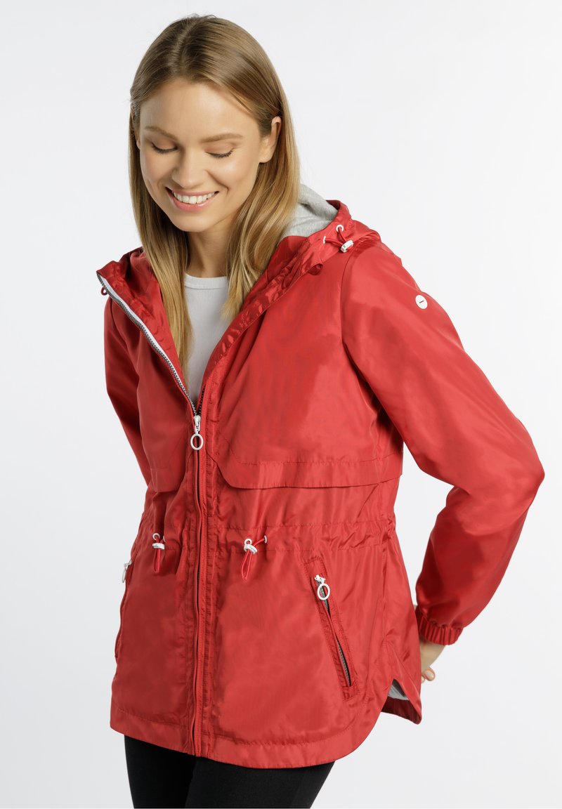 Rote wasserdichte Jacke mit Kapuze, elastischem Zugband in der Taille und mit Reißverschlusstaschen. Sie hat eine glänzende Textur und einen kontrastierenden grauen Innenfutter.
