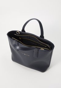 Sac cabas en cuir marine avec deux poignées, détails de fermeture éclair dorés et un compartiment intérieur. Présente un logo embossé à l'avant.