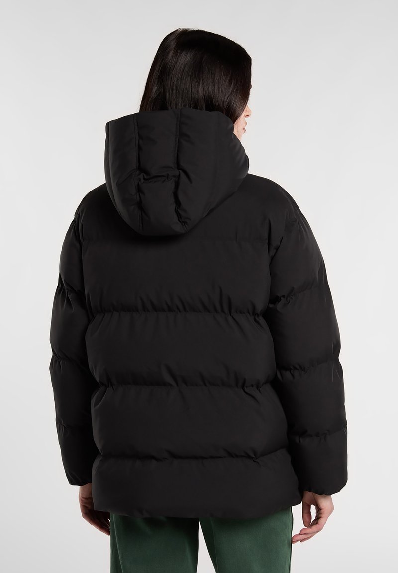 Chaqueta acolchada negra con capucha, que presenta secciones acolchadas y una textura suave. La parte trasera muestra un corte relajado y un dobladillo ligeramente redondeado.
