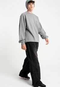 Szary sweatshirt z rękawami typu raglan, w zestawie z luźnymi czarnymi spodniami z bocznymi kieszeniami i czarnymi butami. Model nosi szary dzianinowy beanie.