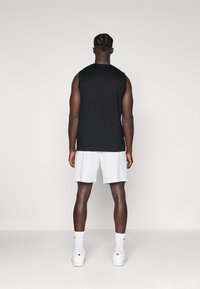 Black sleeveless top and white shorts worn by a person from the back. White sneakers and crew socks complete the athletic outfit.