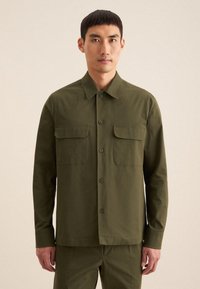 Chemise olive verte à boutons, manches longues, deux poches poitrine, en coton lisse, coupe décontractée, col classique.