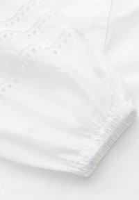 Manche en tissu blanc avec poignet élastique et bordure en dentelle ajourée décorative le long du bord.