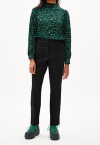 Černý top s dlouhým rukávem a zeleným květinovým vzorem, kombinovaný s dobře padnoucími černými kalhotami a tmavými teniskami se zelenými tkaničkami.