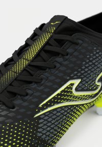 Sapatilha atlética preta com uma superfície texturizada, apresentando um design de destaque em amarelo e atacadores pretos. Inclui um logótipo em destaque e uma silhueta elegante.