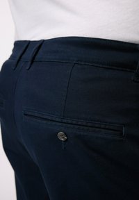 Navyblå byxor med rak design, utrustade med en enda bakficka, sömdetaljer och knäppning. Tillverkade av ett slätt tyg.