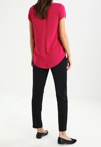 Top fucsia de manga corta con dobladillo redondeado, combinado con pantalones ajustados negros y bailarinas negras. Textura suave, diseño casual.