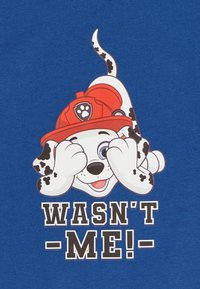 Camiseta azul con un perro de dibujos animados que lleva un casco de bombero, cubriéndose los ojos. El texto debajo dice "¡NO FUI YO!" en letras negras y negritas.