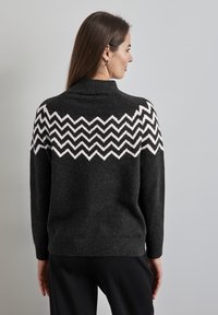 Maglione grigio scuro con colletto alto, caratterizzato da un motivo zigzag bianco e nero sulle spalle e polsini e orlo a coste.