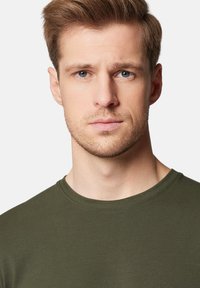 Oliwkowa koszulka z krótkim rękawem, okrągły dekolt, gładka tekstura, dopasowany krój, z detalami przeszycia przy kołnierzu i dolnym skraju.