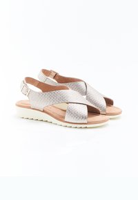 Sandali metallici argento con design a strisce incrociate, cinturino alla caviglia regolabile, tomaia texturizzata e suola bassa bianca. Fodera interna marrone.